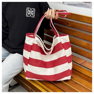 Detail view of a red and white striped canvas tote bag held by a person on a bench
