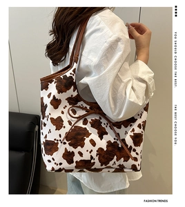Cow print tote bag with brown leather straps and bow detail shown on a female model