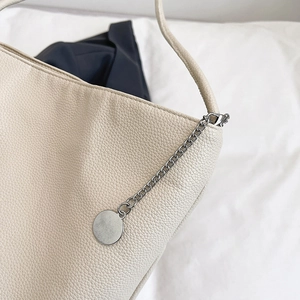 Minimalist beige bucket bag in lychee leather featuring silver chain and round pendant