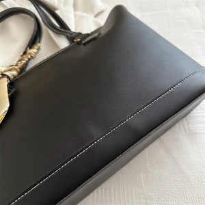 Elegant black tote bag with white contrast stitching and decorative silk scarf handle