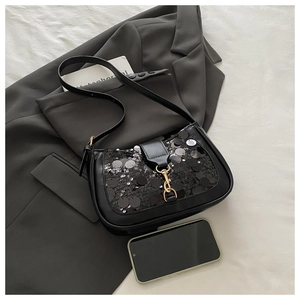 Detail of black sequined shoulder bag with gold metal hook clasp on a grey blazer