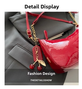 Detail of red patent leather crescent bag with gold chain and cherry charm accessory