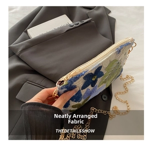 Detail of woven clutch featuring blue floral embroidery and sparkling sequins with gold chain