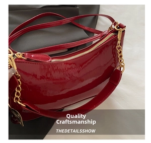Close-up of vibrant red patent leather moon bag featuring shiny gold chain and embossed logo