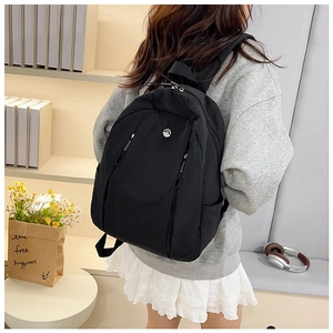 Close-up of black nylon backpack on a person, featuring sleek fabric and round brand logo