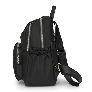 Black nylon quilted backpack with gold zippers and side pockets in a side view profile