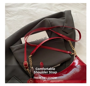 Close-up of a glossy red patent leather shoulder bag with a gold chain and leather strap