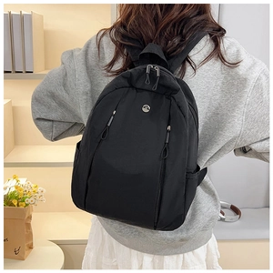 Detail view of lightweight black nylon backpack with circular metal M logo on back