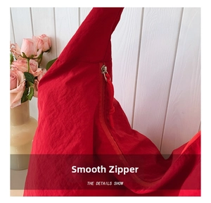 Detail view of smooth red zipper with matching braided cord on lightweight nylon tote bag