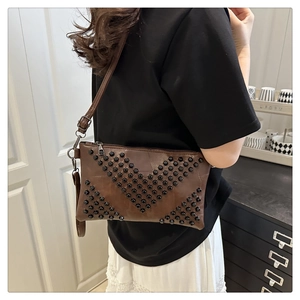 Close-up of brown leather envelope bag with black rivets in V-pattern and silver buckles