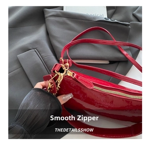 Close-up of red patent leather crescent bag with gold zipper and chain detail