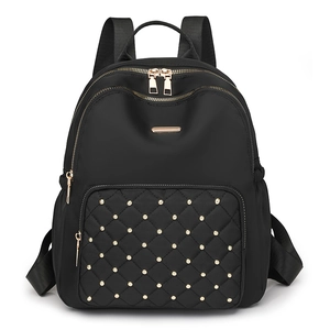 Black nylon backpack with gold studs and quilted front pocket on white background