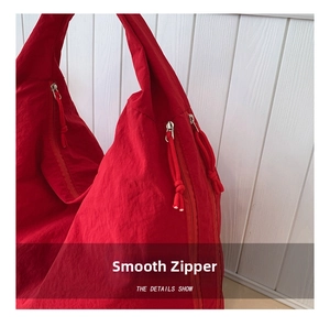 Close-up of red nylon tote bag featuring smooth metal zippers and knotted cord pulls