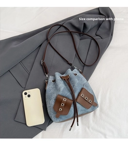 Detailed top view of light blue denim bucket bag with brown leather drawstrings on fabric