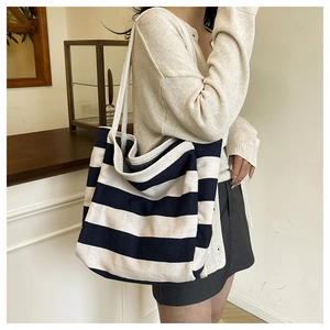 Detail of a large black and white striped canvas tote bag worn on shoulder in minimalist room