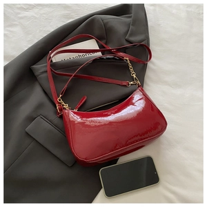 Detail of red patent leather crescent bag with gold chain and strap on a blazer