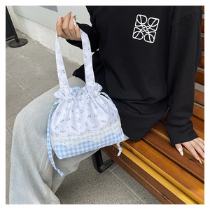 Detail of floral and gingham drawstring bucket bag with lace trim on a wooden bench