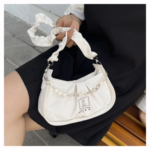 Détail d'un sac à main blanc froncé avec chaîne en perles et poignée plissée sur un banc