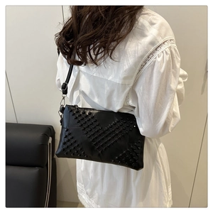 Detail of black leather envelope bag with symmetrical rivet pattern and shoulder strap