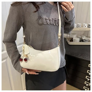 Close-up of white patent leather shoulder bag with a decorative red cherry charm