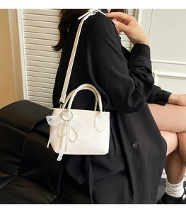Close-up of white lychee leather bucket bag with lace bow and pearl charm detail