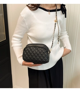 Model wearing a black quilted leather crossbody bag with gold chain and ball adjuster