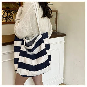 Side view of a large black and white striped canvas tote bag worn by a model