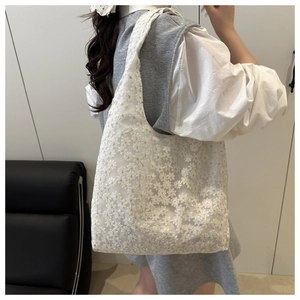 Close-up of white lace tote bag with floral embroidery on a shoulder model