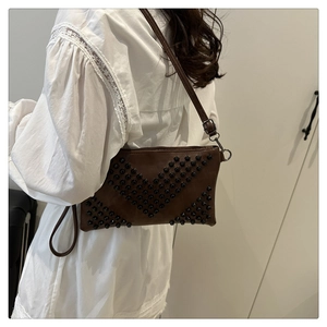 Brown crossbody bag with black stud details shown on model wearing white shirt