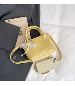 Detail of yellow leather mini square bag with pearl bow and embossed fashion text