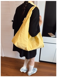 Detail of a yellow nylon tote bag with pleated texture and knot zipper pull on shoulder