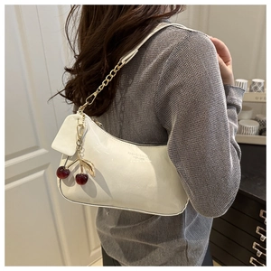 Detail of white patent leather shoulder bag with cherry pendant and metal chain strap
