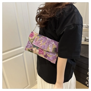 Dettaglio del ricamo floreale di paillettes su una pochette in paglia con catena oro