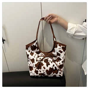 Dettaglio della borsa tote con stampa mucca, manici in pelle marrone e fiocco decorativo