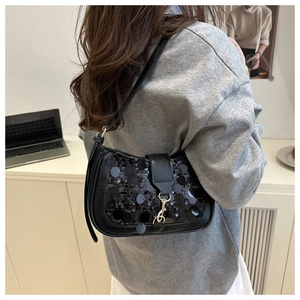 Detail of black sequined shoulder bag with gold metal buckle on a minimalist office desk