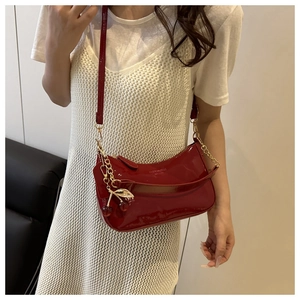 Detail of red patent leather shoulder bag with cherry charm on a white dress
