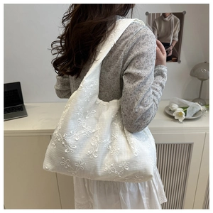 Detail view of white lace flower embroidery on large canvas tote bag carried by a model