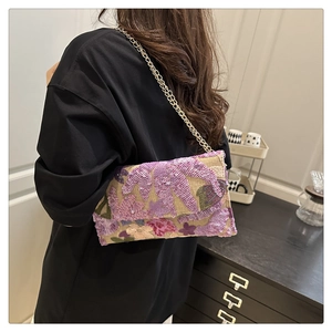 Dettaglio di ricamo floreale con paillettes e catena dorata su borsa beige intrecciata