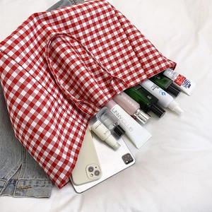 Grand sac cabas en toile à carreaux rouges vue de dessus sur un tissu blanc avec accessoires