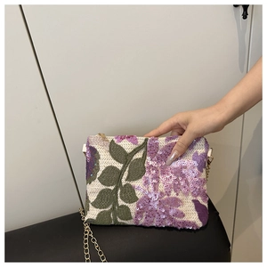 Detailed view of straw clutch with purple sequin flowers and green leaf embroidery
