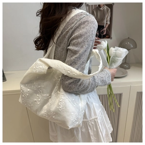 Detail of white floral lace embroidery on a sheer tote bag with wide shoulder strap