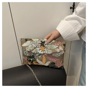 Dettaglio del ricamo floreale in paillettes su borsa a busta in paglia con catena