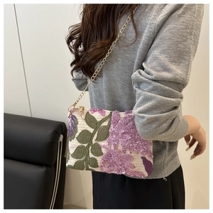 Detail of sequin floral embroidery and gold chain strap on a woven crossbody bag
