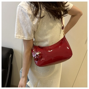Detail of red patent leather shoulder bag with decorative golden cherry pendant and zipper