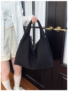 Detail of a large black nylon tote bag with drawstring sides held by a model