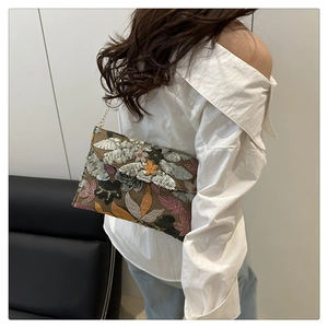 Dettaglio di ricamo e paillettes su pochette etnica con tracolla a catena oro