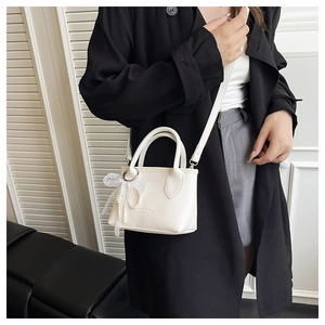 Detail of off-white lychee leather bag with lace trim and pearl bow pendant decoration