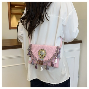 Detail of pink woven straw bag featuring bohemian beaded disc and fringe tassels