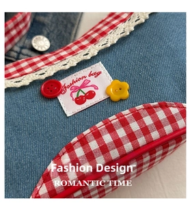 Detail of denim bag with cherry patch, lace trim, and red plaid piping accents