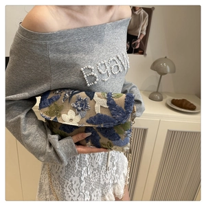 Dettaglio ricamo floreale e paillettes su pochette in paglia intrecciata con catena d'oro